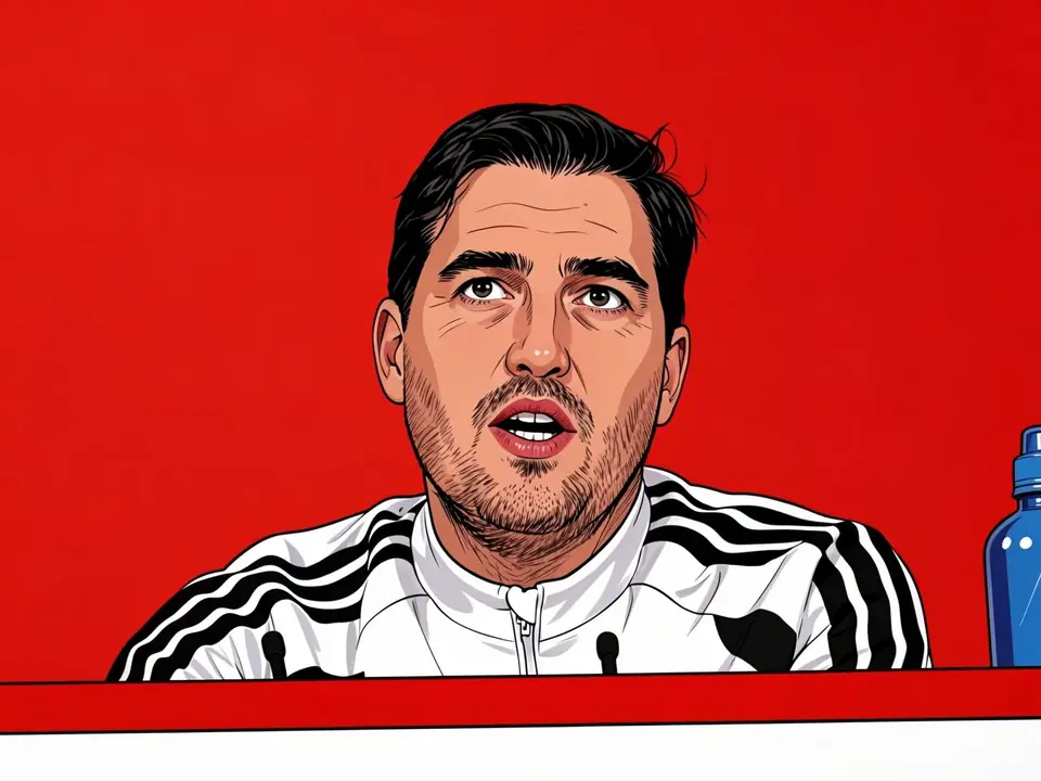 Liverpool manager Iraola speaks at a press conference wearing a white Adidas tracksuit with black stripes against a red background.