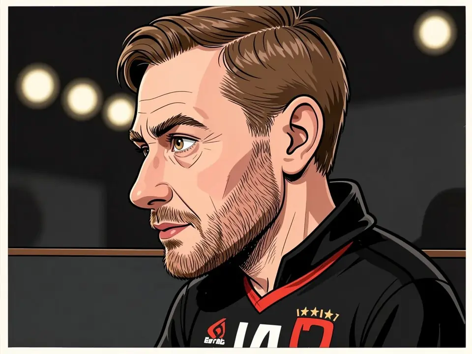 Scott Gordon in schwarzem Traktor-Trikot mit rotem Kragen. Der Cheftrainer sitzt auf der Bank.