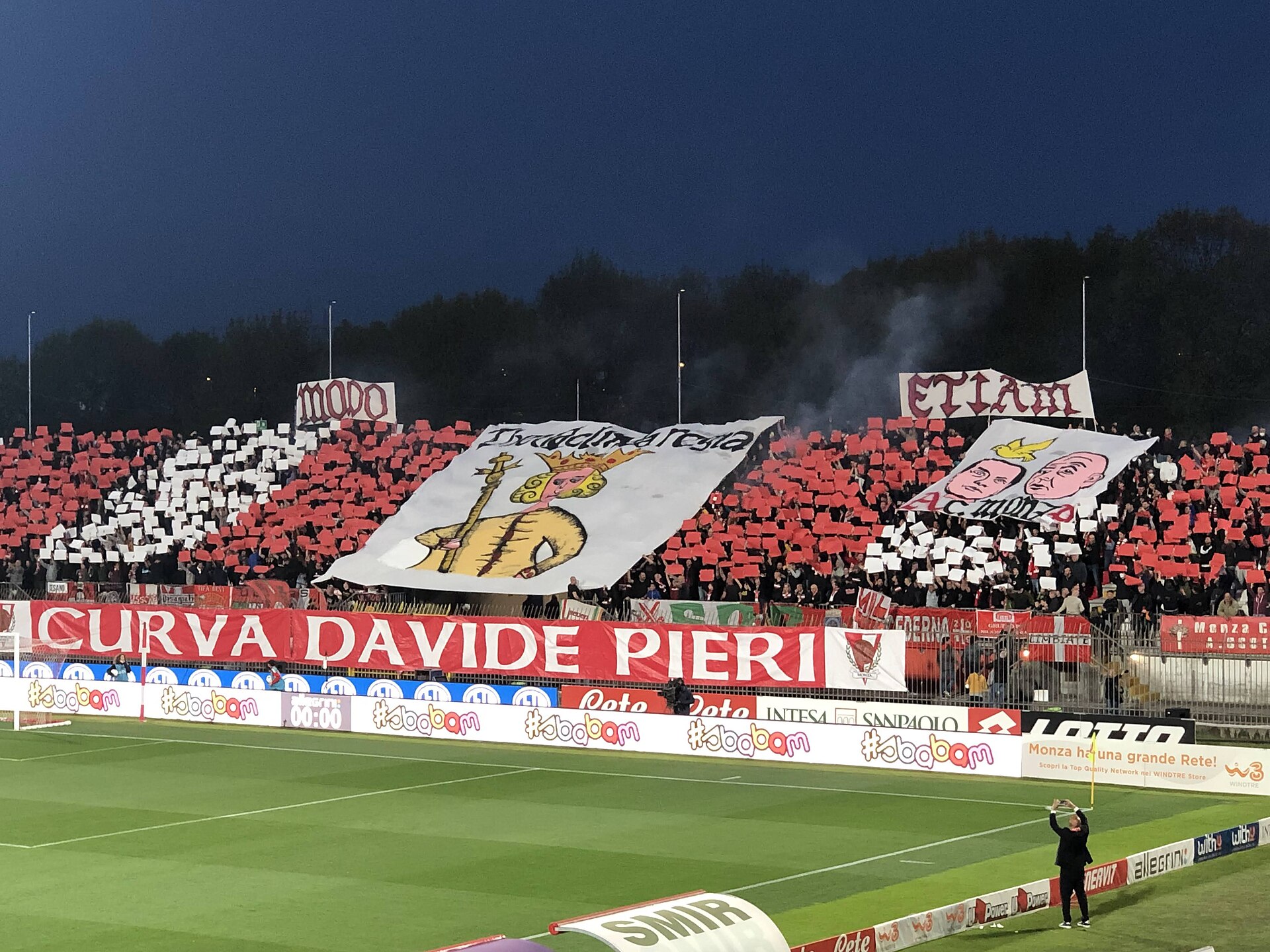 A choreography by AC Monza fans in a Serie B game against Brescia. Theodelinda is represented in the middle, with the words "MODO" and "ETIAM" on top. The banner on the right shows a dove on top of drawings of Silvio Berlusconi and Adriano Galliani's heads.