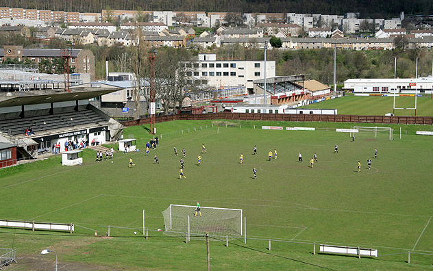 Gala Fairydean Football ground Viewed on a Sunday and most likely to be a youths game. Gala Rugby Football ground is next door and the housing in the background is at Langlee. The football ground is bisected by a grid line over the width of the pitch.