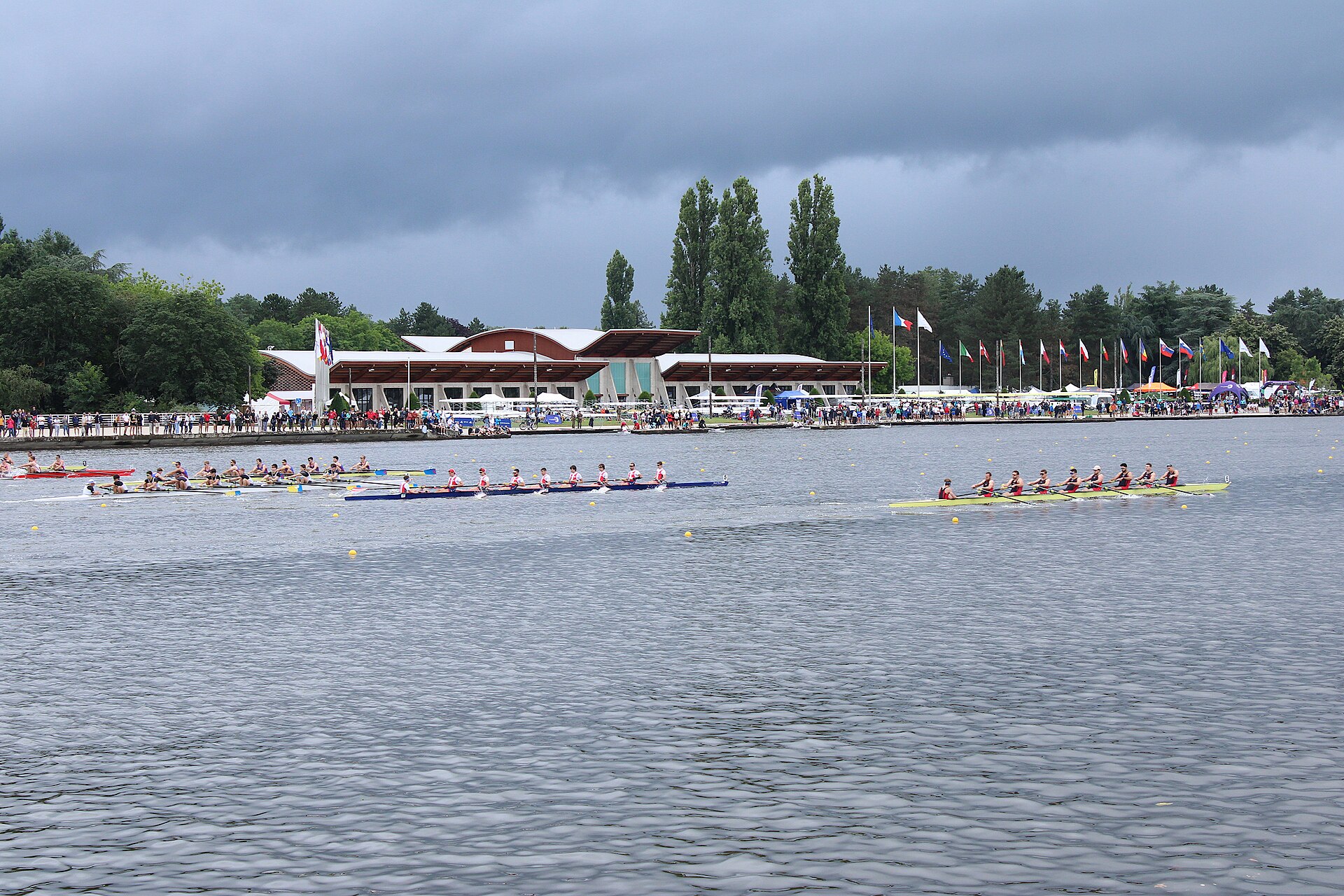 Championnats de France d'aviron J16 et critérium handi-valide J16, sprint senior et para-aviron 2024, côté rive droite, territoire communal de Vichy (Allier, Auvergne-Rhône-Alpes, France). Le Palais du Lac, utilité historique pour les compétitions de ce type, est en arrière-plan.