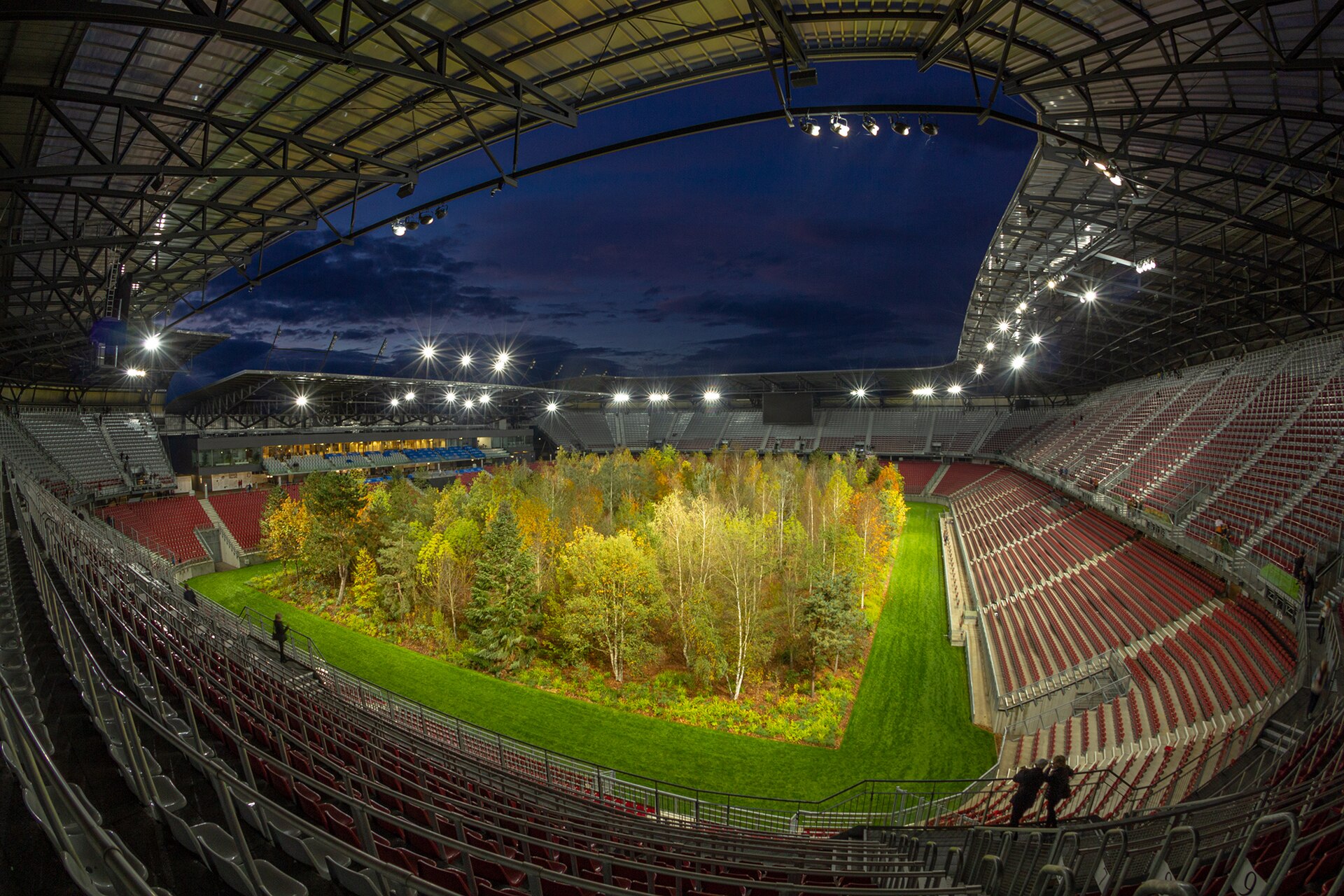 For Forest. The Unending Attraction of Nature” was a temporary art intervention by Klaus Littmann in the football arena of Klagenfurt, Austria. The project was based on the pencil drawing “The Unending Attraction of Nature” by Max Peintner from the 1970s, which shows a small forest in a crowded sta