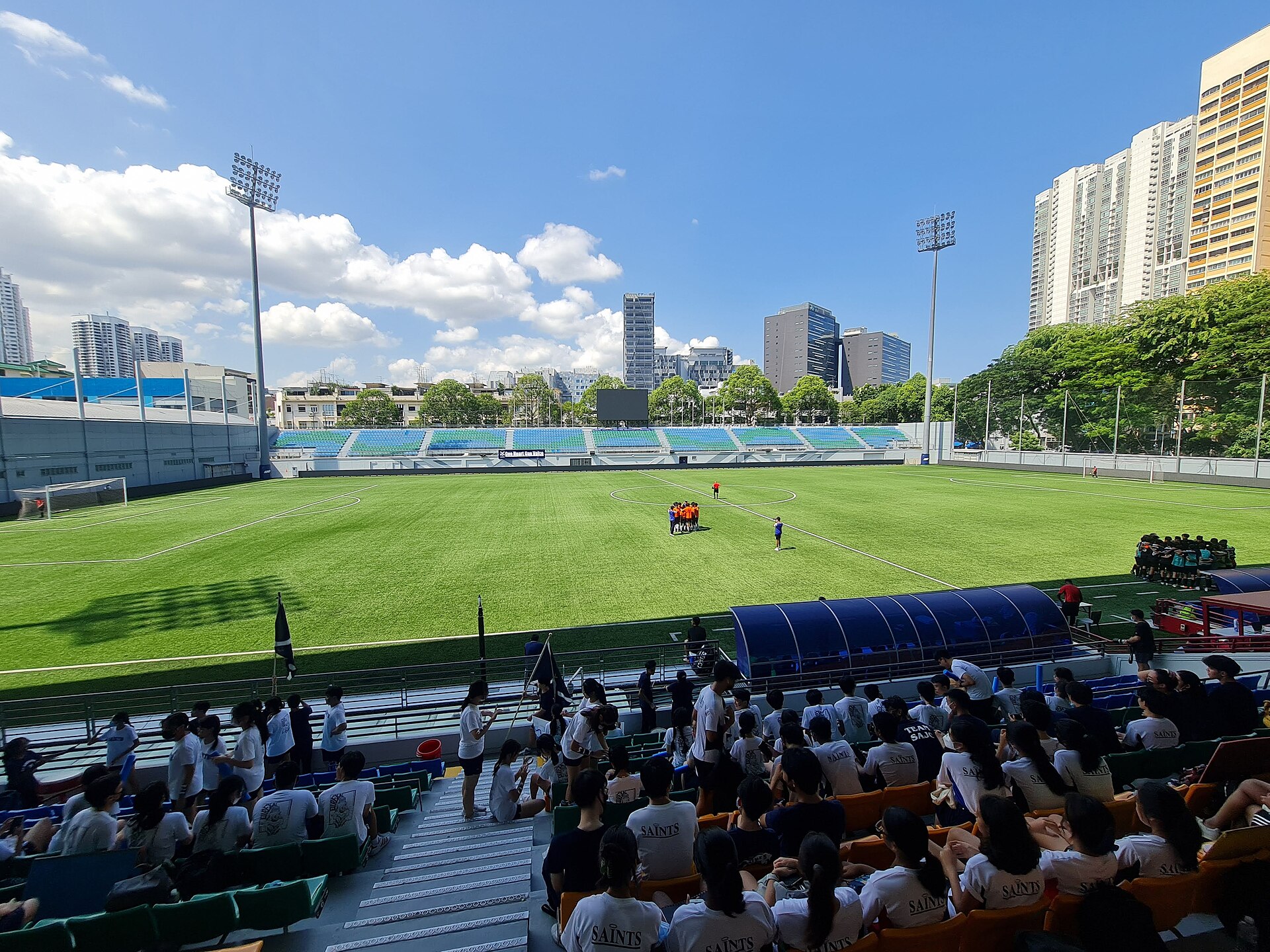 Jalan Besar Stadium during the 2022 National School Games A-Division Football Semi-Final match played by St. Andrew’s Junior College against Anglo-Chinese Junior College. The image depicts St. Andrew student supporters watching their own school’s team (in orange jerseys) immersing in a pre-game hudd